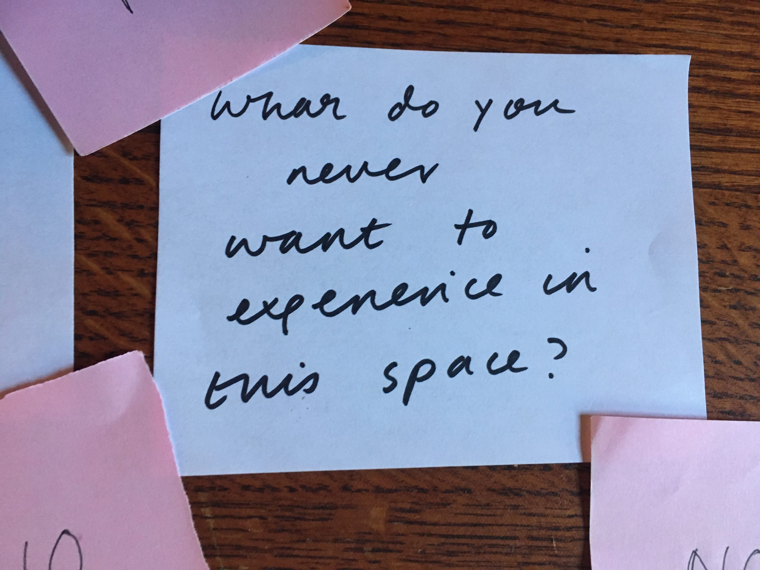 A scrap of white paper surrounded by pink Post-It notes reads in handwriting, "what do you never want to experience in this space?" 